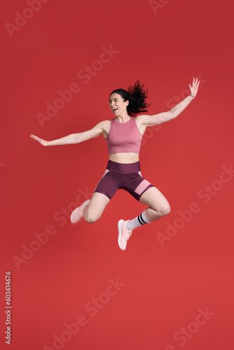 Excited determined strong sportswoman, smiling and stretching her body while jumping, red background