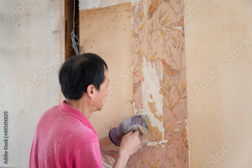 Man removing old style vintage floral wallpaper inside an old house. Home renovation project. Auckland.