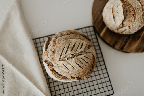 Home made sourdough bread. Resting on cooling rack and wooden board. On the left side there is a linen napkin. Minimalism in a horizontal flat lay image. 
