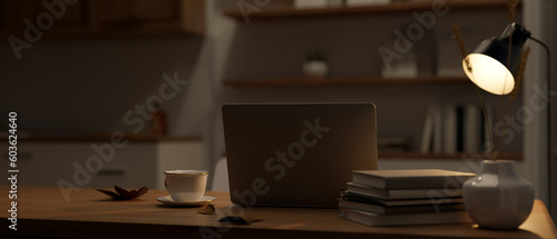 Modern workspace at night in a dark room with laptop, table lamp, and decor on a table