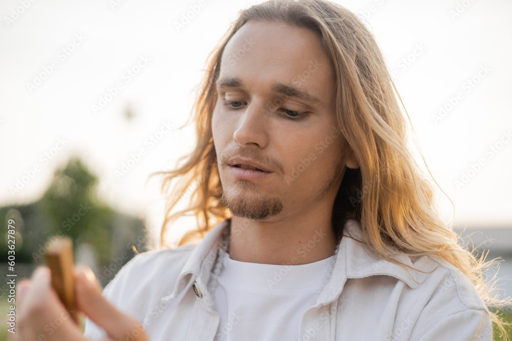 portrait of young man with long fair hair holding blurred palo santo stick outdoors portrait of young man with long fair hair holding blurred palo santo stick outdoors