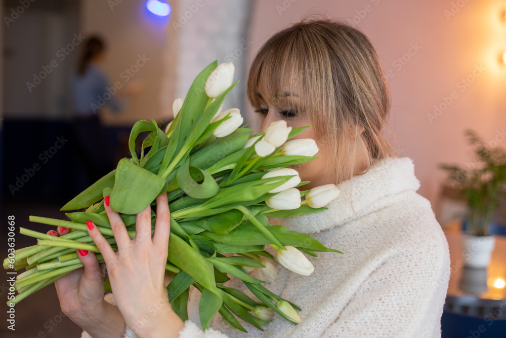 Obraz premium Portrait of a young girl with blond hair smelling white tulips in room inside where is full length mirror background