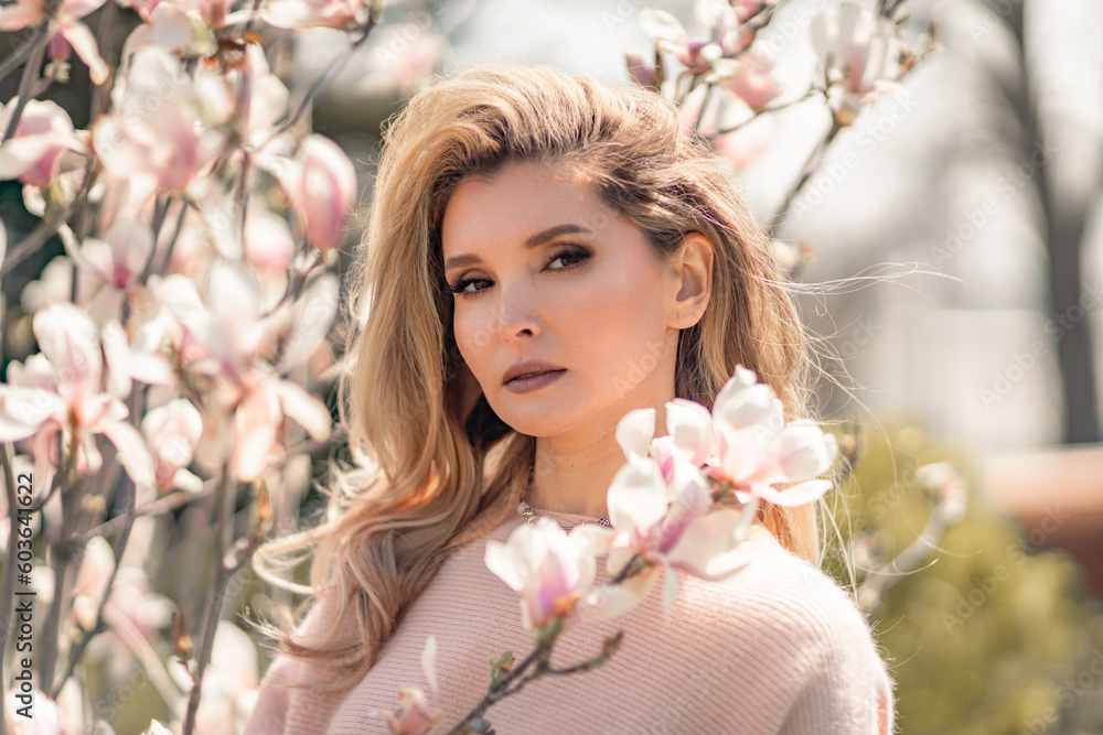 Portrait of a beautiful happy middle aged woman enjoying the smell in a blooming spring garden. Beautiful magnolia bushes, large flowers.