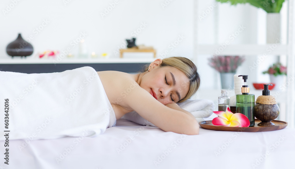 Portrait shot of Millennial Asian young beautiful relaxing resting nude naked woman laying lying down smiling look at camera on comfortable massage bed under clean white towel waiting for masseuse