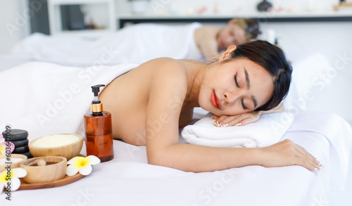 Portrait shot of Millennial Asian young beautiful relaxing resting nude naked woman laying lying down smiling look at camera on comfortable massage bed under clean white towel waiting for masseuse