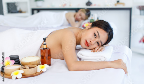 Portrait shot of Millennial Asian young beautiful relaxing resting nude naked woman laying lying down smiling look at camera on comfortable massage bed under clean white towel waiting for masseuse