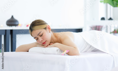 Portrait shot of Millennial Asian young beautiful relaxing resting nude naked woman laying lying down smiling look at camera on comfortable massage bed under clean white towel waiting for masseuse