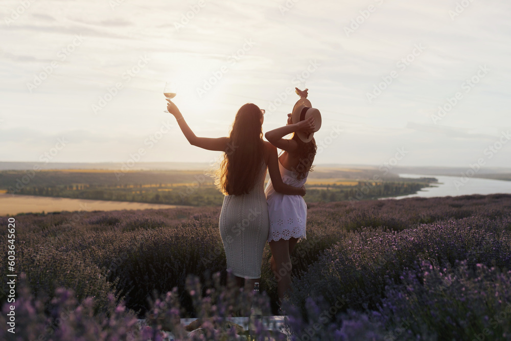 Young women having a picnic in the lavender field with wine at sunset.