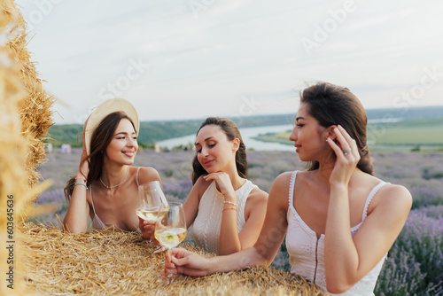 Obraz na płótnie Three women sitting on hay bales in a field and clinking wine glasses. w salonie
