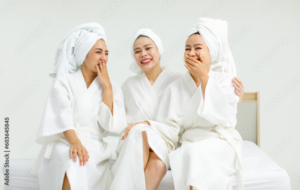 Millennial three Asian female customers friends in white clean bathrobes and towels have appointment at massage resort sitting on chair chit chat talking having conversation together before massaging Millennial three Asian female customers friends in white clean bathrobes and towels have appointment at massage resort sitting on chair chit chat talking having conversation together before massaging