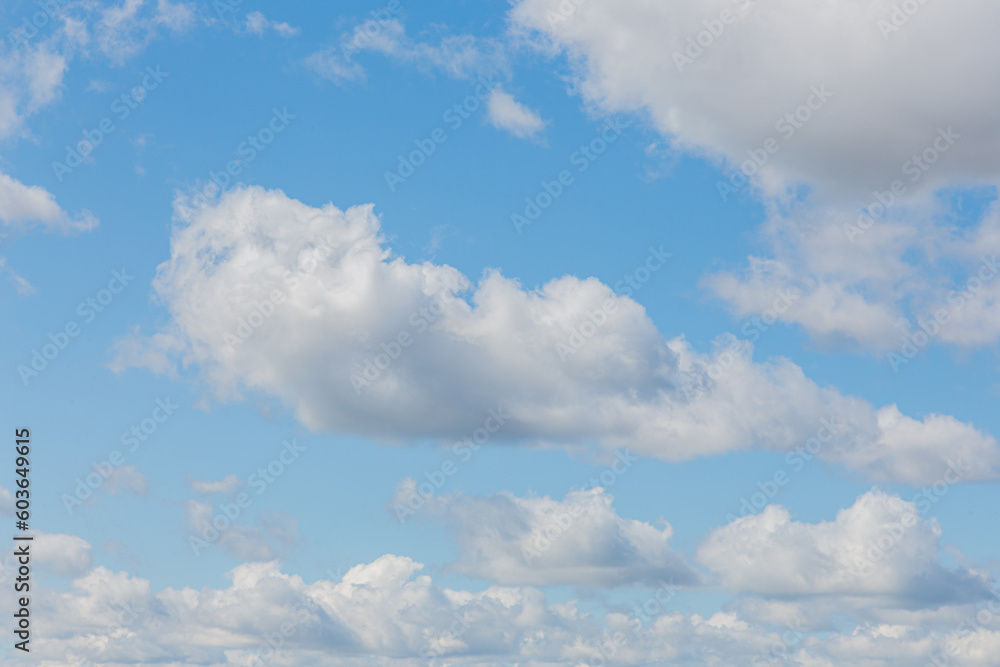 White fluffy clouds on a summer blue sky in cartoon style for background or wallpaper design. The background is white of round clouds in a blue sky. White fluffy clouds on a summer blue sky in cartoon style for background or wallpaper design. The background is white of round clouds in a blue sky.