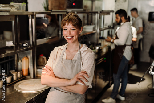 Smiling young blonde woman business owner in apron looking at camera in cafe kitchen
