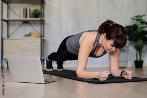 young woman watching online training on laptop and doing fitness exercises