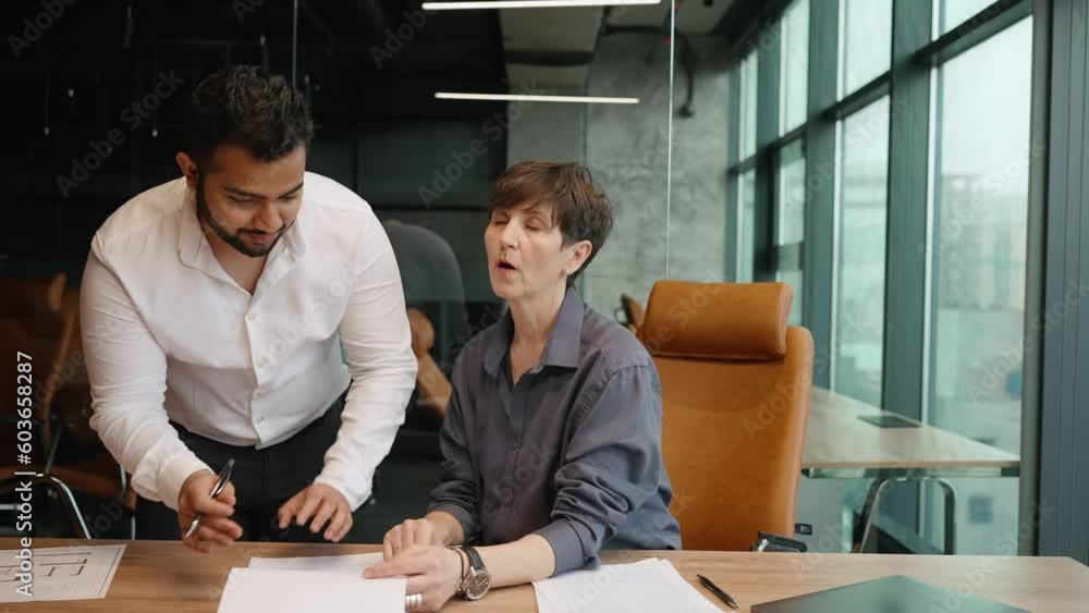 Handsome multinational man and woman colleagues discussing work and signing documents in office Handsome multinational man and woman colleagues discussing work and signing documents in office