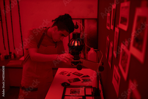 Young photographer using special equipment to make photo in darkroom with red light photo