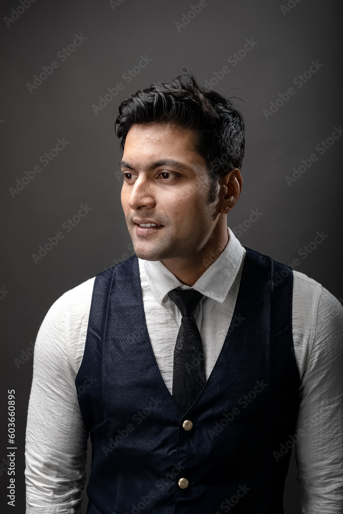 Studio shot of cheerful, young, handsome Indian male model in formal wear wearing white shirt, black tie, black coat against grey background. Male model. Fashion Portrait. Studio shot of cheerful, young, handsome Indian male model in formal wear wearing white shirt, black tie, black coat against grey background. Male model. Fashion Portrait.