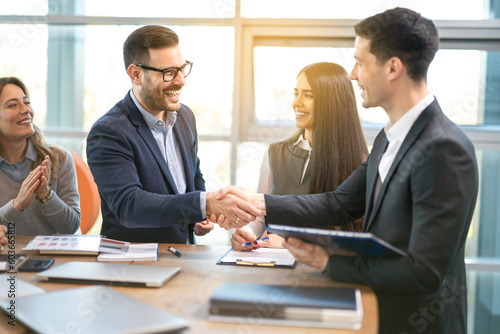 Wallpaper Mural Executive director congratulating his colleague the new position in the company with smiling members of their team around table in the office. Torontodigital.ca