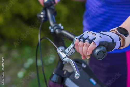 View of female hand in sports gloves and wristwatch on handlebars of bicycle. 