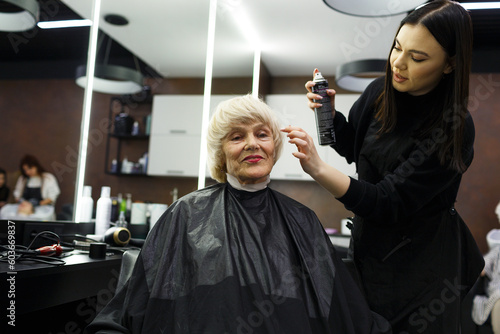 Portrait of an elderly woman visiting a professional hairdresser. An experienced hairdresser does hair styling for a client.