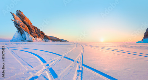 Car tire tracks (trail) in fresh snow - Ogoy island on winter Baikal lake with transparent cracked blue ice at sunrise - Baikal, Siberia, Russia