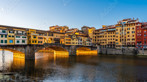 UNESCO site bridge Ponte Vecchio with golden arches in Florence early in the morning sunlight.