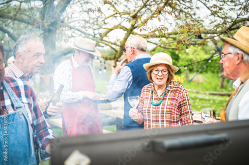 Group of different elderly people preparing barbecue and sipping wine and beer, preparing a lunch and an outdoor party in the garden, concept of healthy and happy elderly people