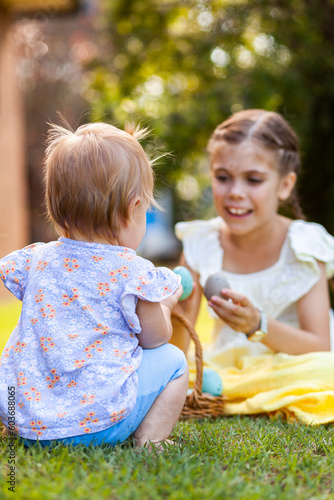 Toddler with older girl sitting on grass with basket of Easter eggs photo