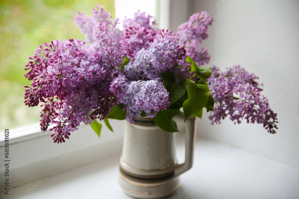 Bouquet of blooming lilac in a vase on the windowsill by the window Bouquet of blooming lilac in a vase on the windowsill by the window