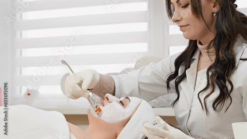 Cosmetology session: a young woman receives a medical mask on her face in a beauty salon. Video for healing skin and enhancing beauty. A professional cosmetologist gently applies the cream with menzel photo