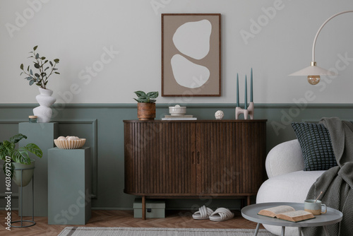 Fotografiet Warm and cozy composition of spring living room interior with mock up poster frame, wooden sideboard, white sofa, green stand, base with leaves, plants, stylish lamp