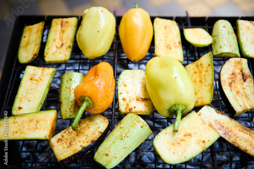 Top view fresh marinated seasoned bell peppers and slices of zucchini grilling on grate over charcoals in the barbecue grill. BBQ party. Preparing delicious food outdoor. Weekend leisures. Picnic