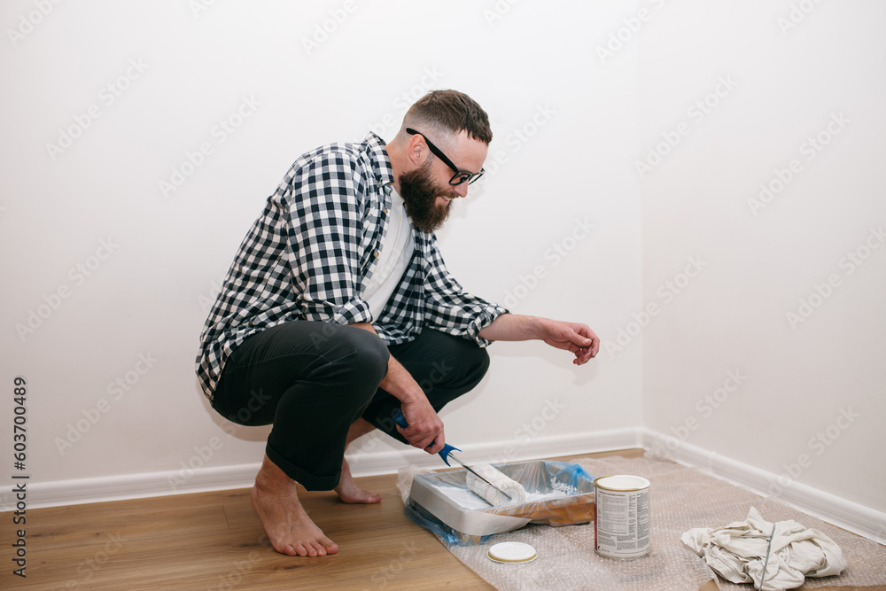 A young attractive man makes repairs in his own apartment and paints the walls white. Apartment renovation concept A young attractive man makes repairs in his own apartment and paints the walls white. Apartment renovation concept