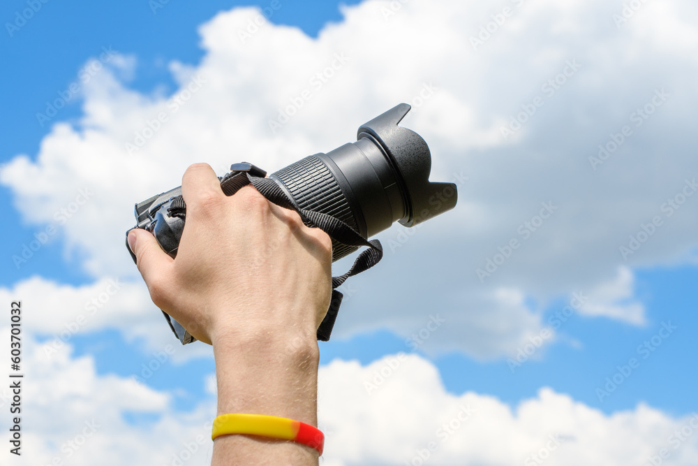 Dłoń trzymająca aparat fotograficzny na niebieskim tle chmur na niebie  - obrazy, fototapety, plakaty 