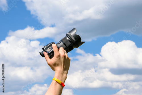 Dłoń trzymająca aparat fotograficzny na niebieskim tle nieba. Chmury wychodzące z aparatu