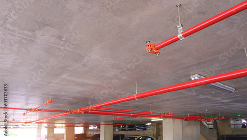 Selective focus at sprinkler with red fire protection water pipeline system on concrete ceiling inside of parking garage building