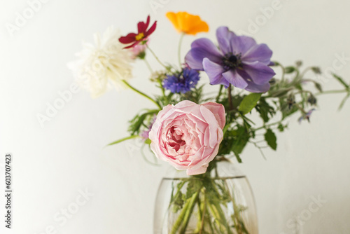 Stylish colorful flowers bouquet on rustic wall background. Beautiful summer wildflowers  anemones and roses in vase gathered from garden  floral arrangement in modern room in home