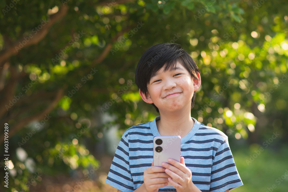 Happy Asian child playing game on mobile phone in the park outdoor Happy Asian child playing game on mobile phone in the park outdoor