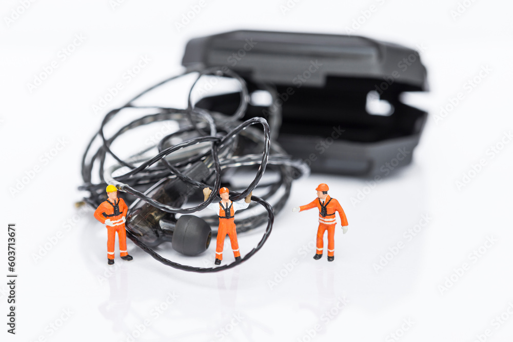 Tangled earphones cable with miniature worker isolate on white background, worker fixing messy wire Tangled earphones cable with miniature worker isolate on white background, worker fixing messy wire