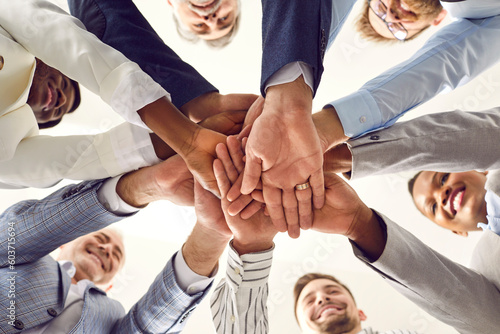 Diverse business team standing together and stacking hands. Happy senior and young mixed race multiethnic people pile up their hands and smile. Bottom view, shot from below. Teamwork concept