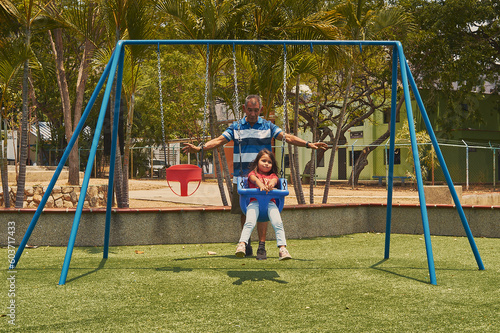 grandfather taking care of his granddaughter, grandfather taking care of his granddaughter playing in an outdoor park, on a sunny morning, in the city of San Diego, Carabobo state. photo