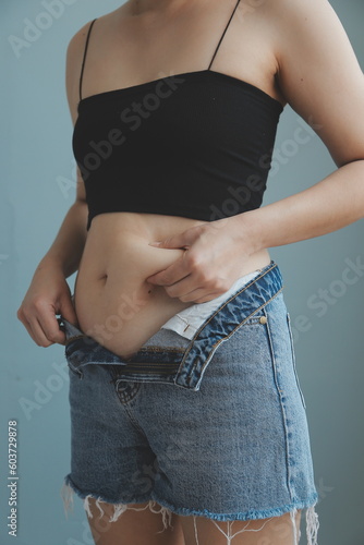 Close up of a belly with scar from c-section and abdominal fat. Women's health. A woman dressed up in sportswear demonstrating her imperfect body after a childbirth with nursery on the background.