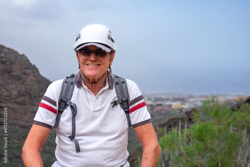 Smiling senior hiker man wearing helmet walking on mountain enjoying a trekking day - Carefree climbing tourist in holidays and healthy lifestyle - Freedom, health, sport concept Smiling senior hiker man wearing helmet walking on mountain enjoying a trekking day - Carefree climbing tourist in holidays and healthy lifestyle - Freedom, health, sport concept