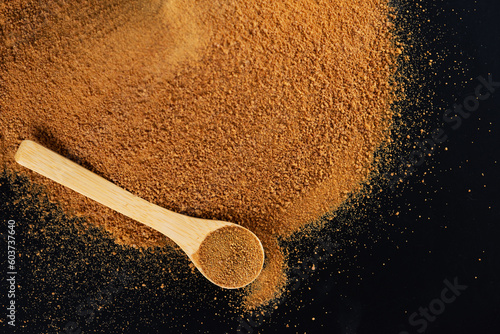 Pile unrefined cane brown sugar Panela with a wooden spoon on a black.