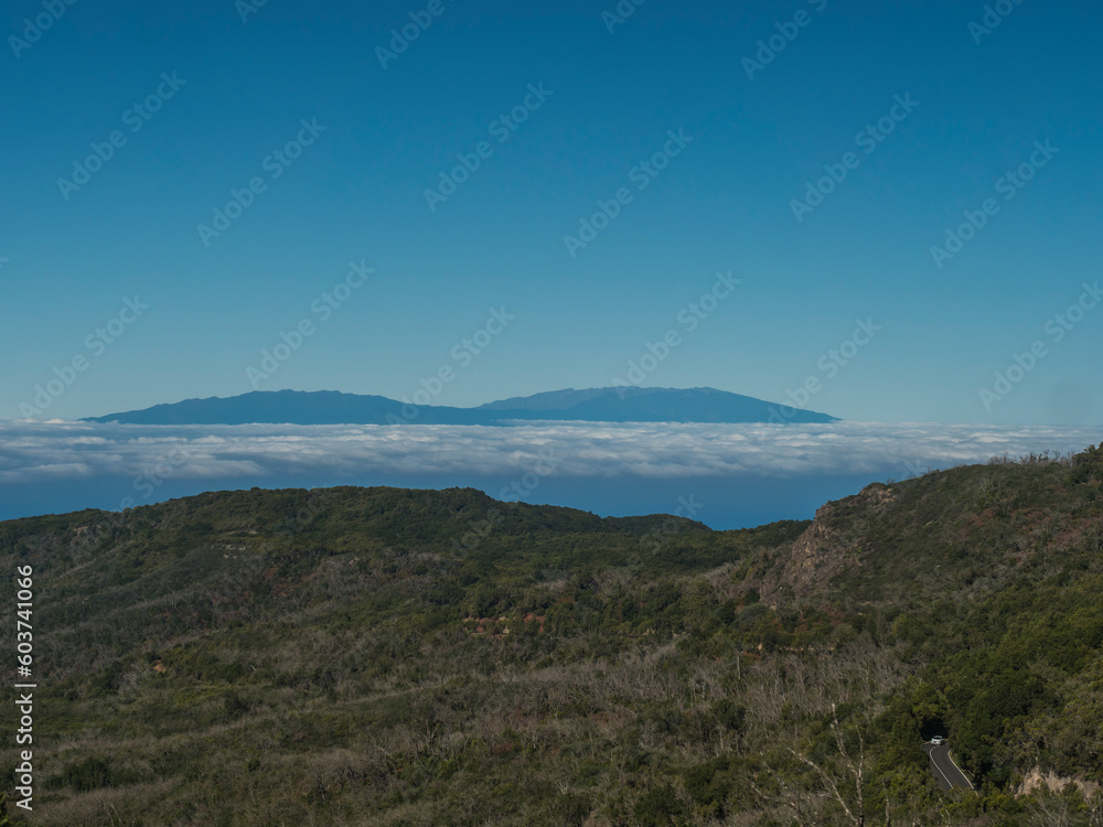 Fototapeta premium View on La Palma island seen from trail to Alto de Garajonay at Garajonay National Park. White clouds and blue sky above. La Gomera, Canary Islands, Spain, Europe.