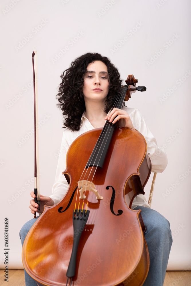 Woman playing violin cello while sitting on chair Woman playing violin cello while sitting on chair