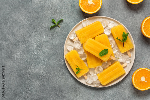 Orange popsicles, gray concrete background. Frozen orange juice on a stick. Summer refreshing and cooling dessert. Top view, flat lay, copy space