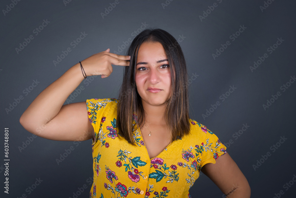 Unhappy blonde woman curves lips and makes suicide gesture, tired of everything, shoots in temple with hand, isolated against studio background. Upset female gestures indoors, tries kill herself Unhappy blonde woman curves lips and makes suicide gesture, tired of everything, shoots in temple with hand, isolated against studio background. Upset female gestures indoors, tries kill herself