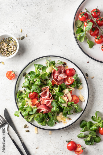 Green salad with ham or prosciutto, corn salad leaves, tomatoes and cheese. Healthy diet lunch on white marble background top view flat lay