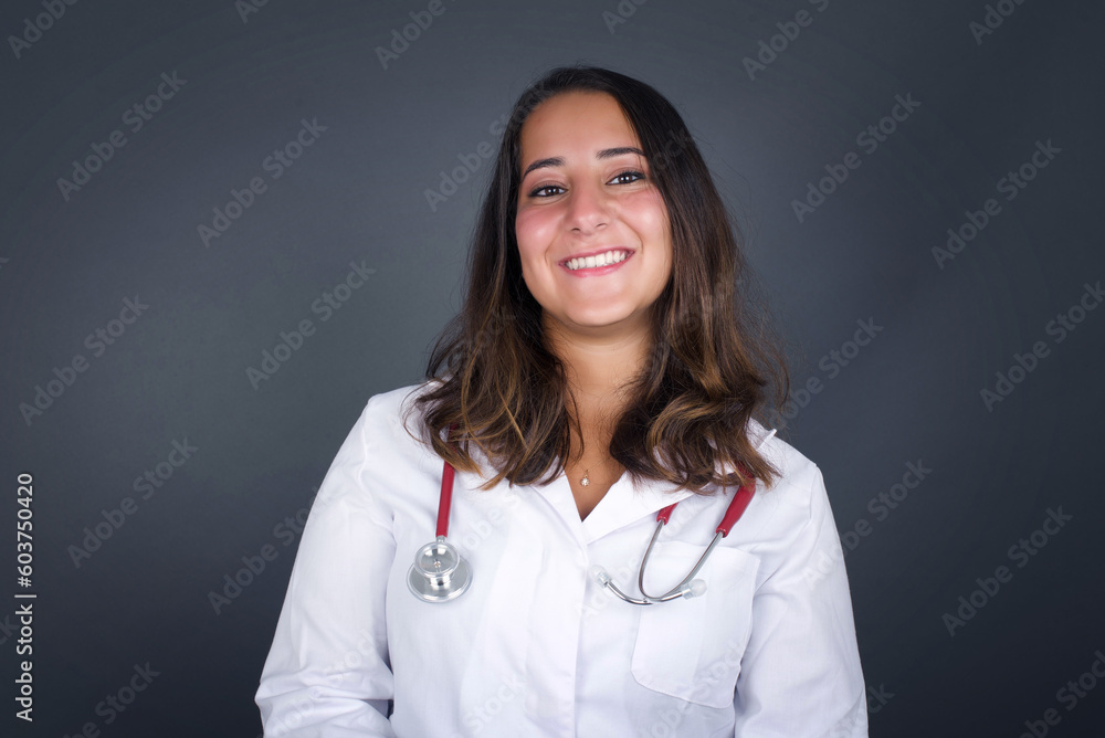 Beautiful smiling brunette female with broad smile, shows white teeth, wears casual t shirt, stands over gray studio wall rejoices having day off. Woman standing indoors. Beautiful smiling brunette female with broad smile, shows white teeth, wears casual t shirt, stands over gray studio wall rejoices having day off. Woman standing indoors.