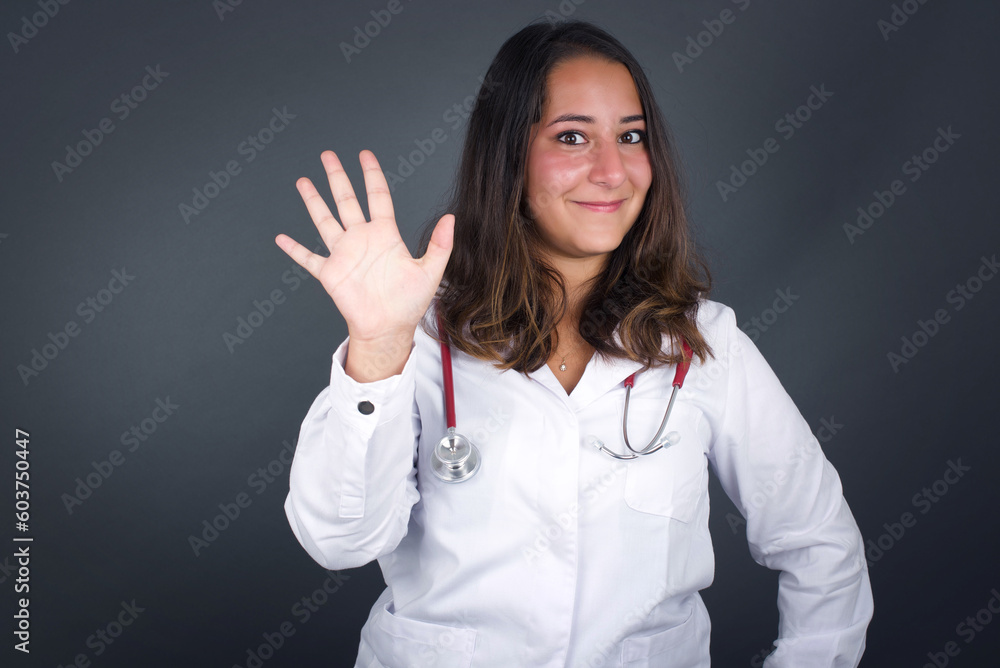 Young woman standing against gray wall showing and pointing up with fingers number five while smiling confident and happy. Young woman standing against gray wall showing and pointing up with fingers number five while smiling confident and happy.